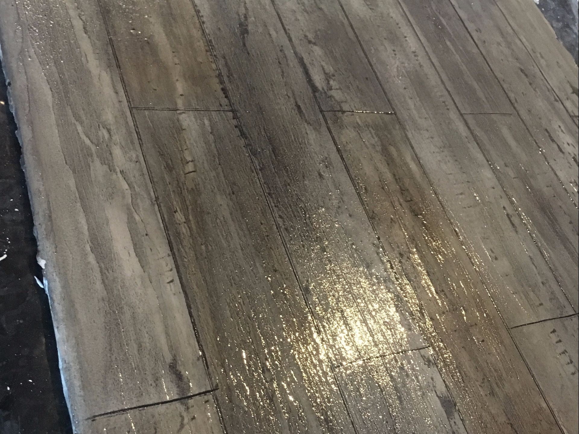 Wet, gray wood-look flooring with visible water droplets, reflecting light.