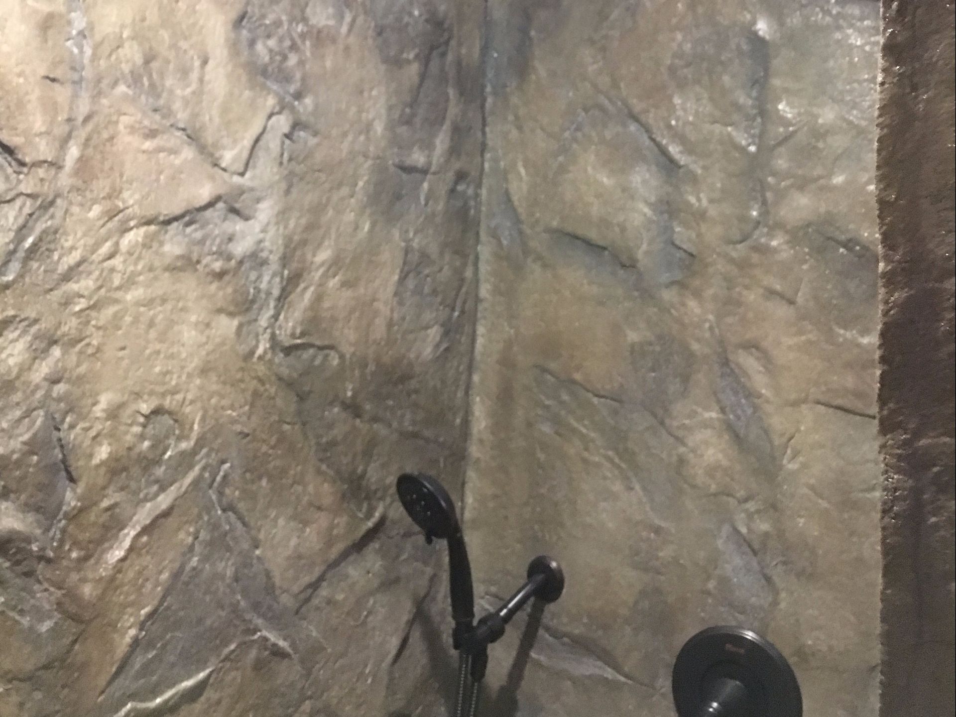 Shower with textured stone-like walls, a black showerhead, and faucet fixtures.