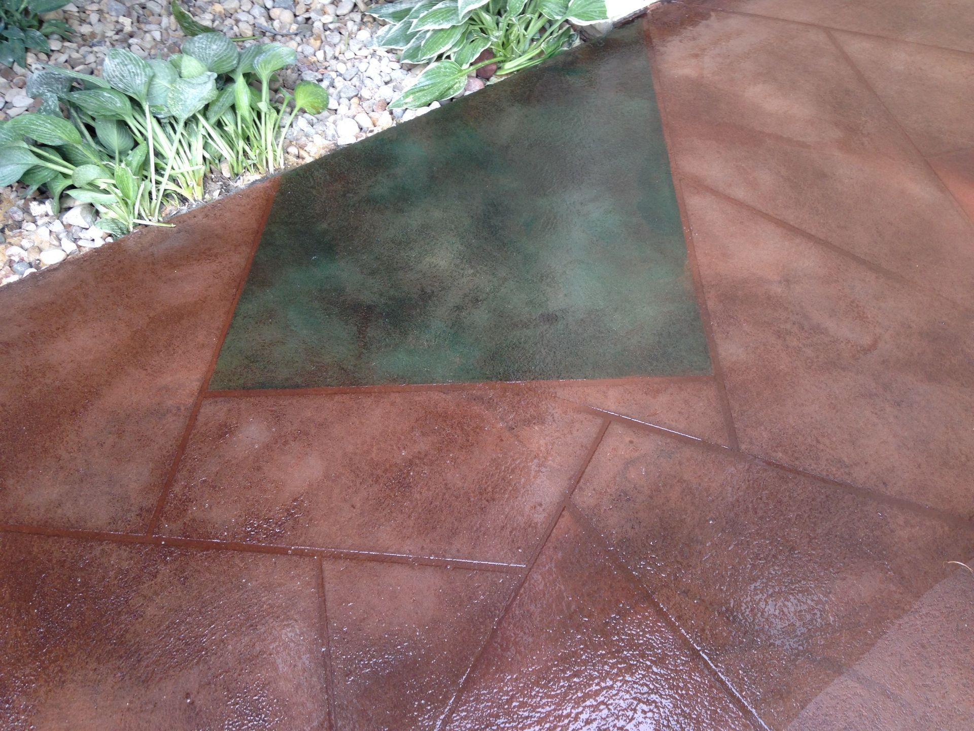 Brown and green stained concrete patio with a garden in the background.