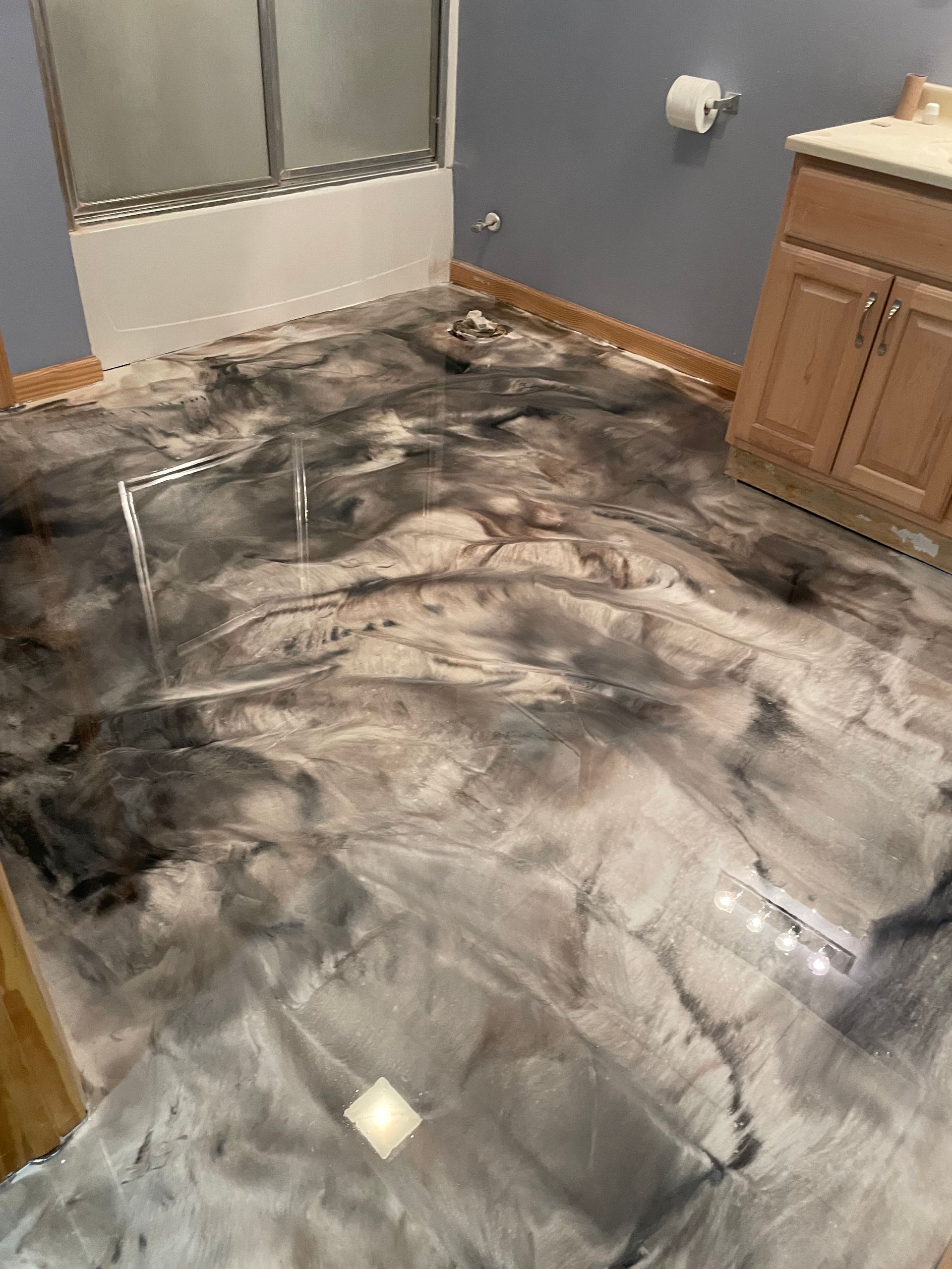 Bathroom floor with a metallic epoxy finish, featuring swirls of black, gray, and silver.