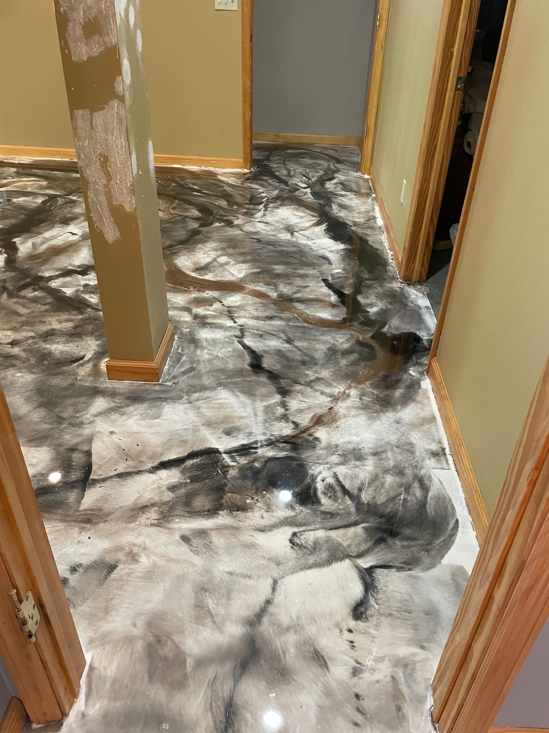 Metallic epoxy flooring in shades of silver, gray, and black, resembling stone, with a column and doorways.