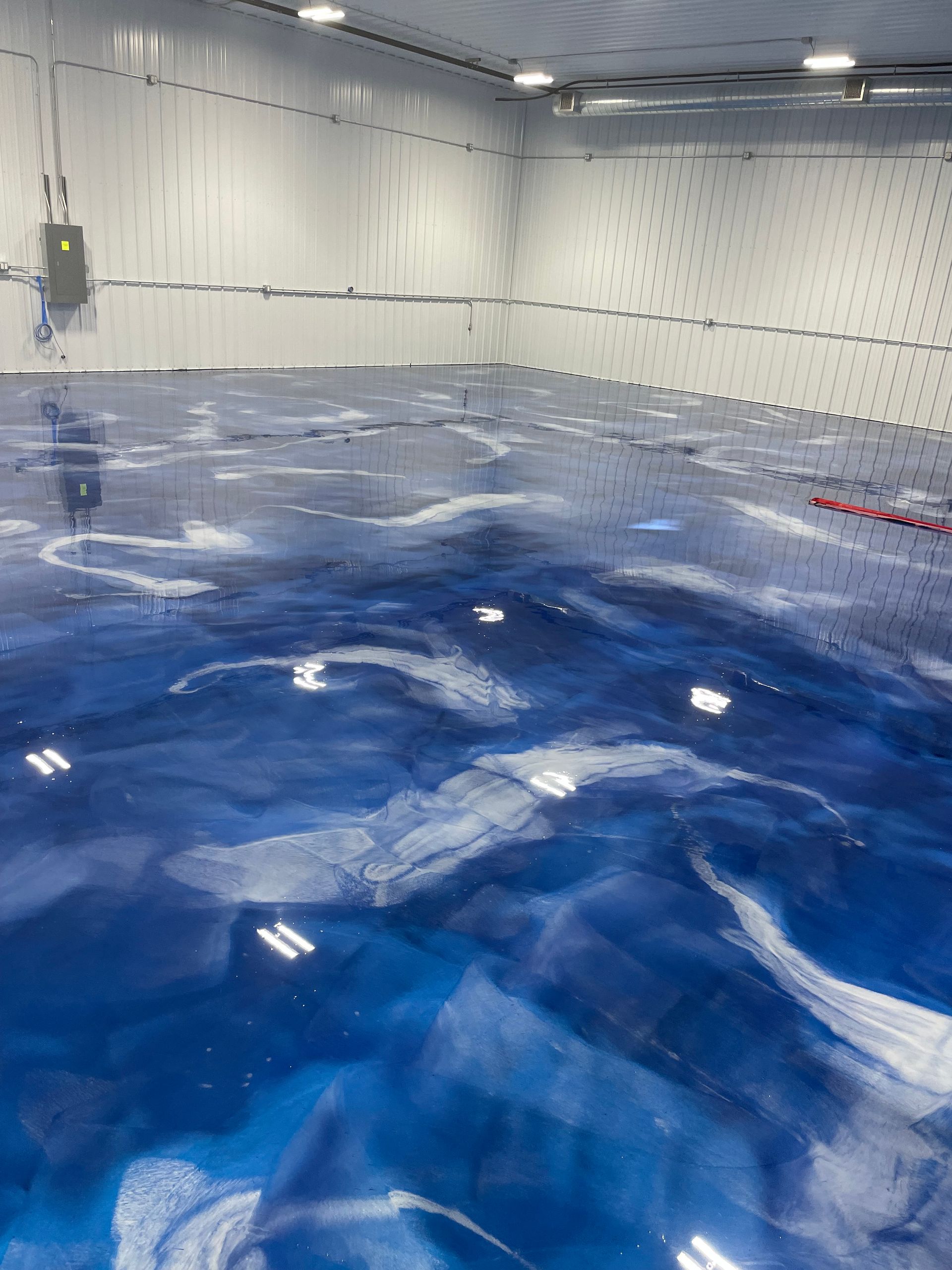 Blue epoxy floor with white swirls, resembling water, in a large, white-walled room.