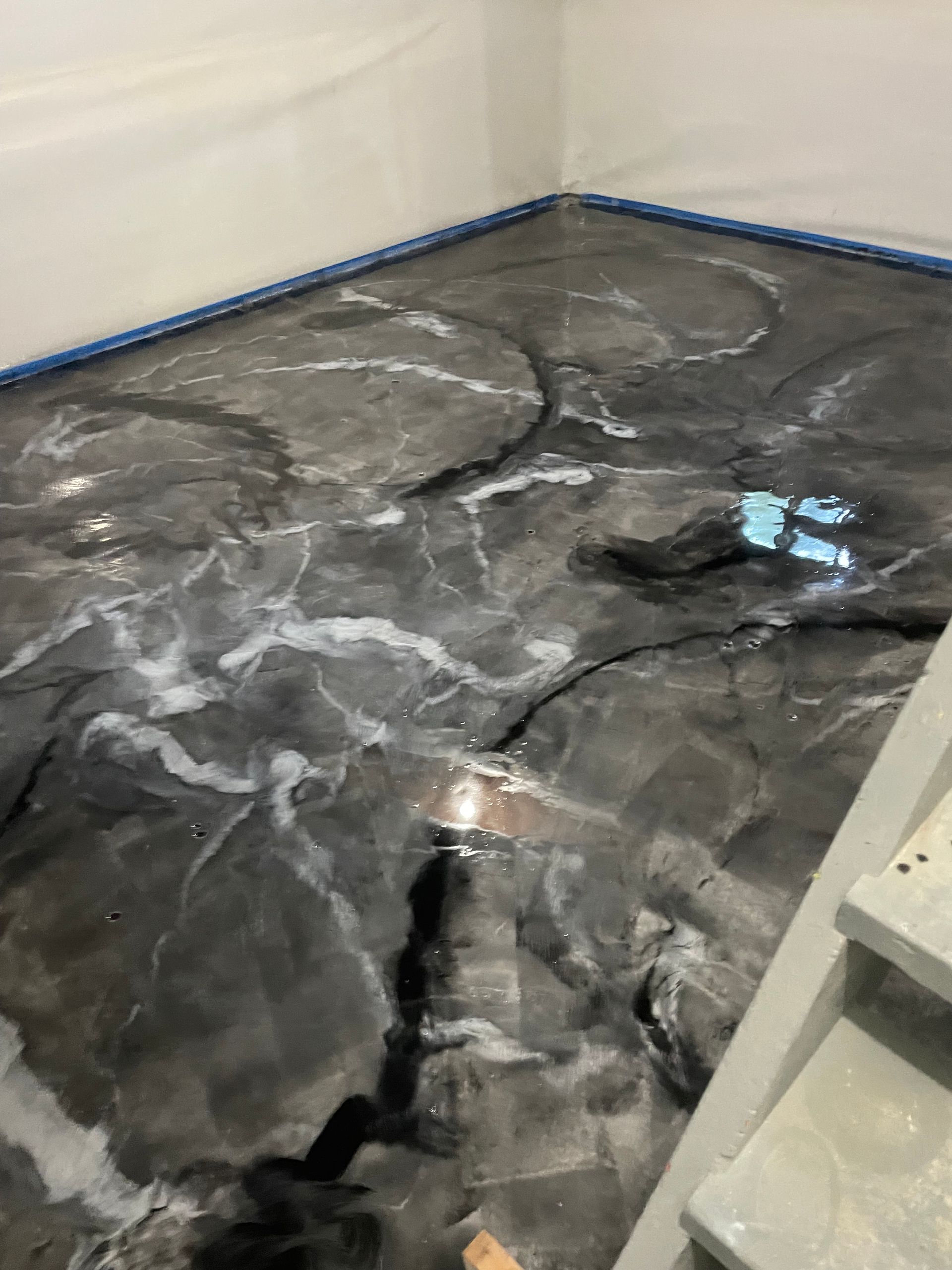 Epoxy floor with dark gray, white swirls, reflecting light. Corner of a room.