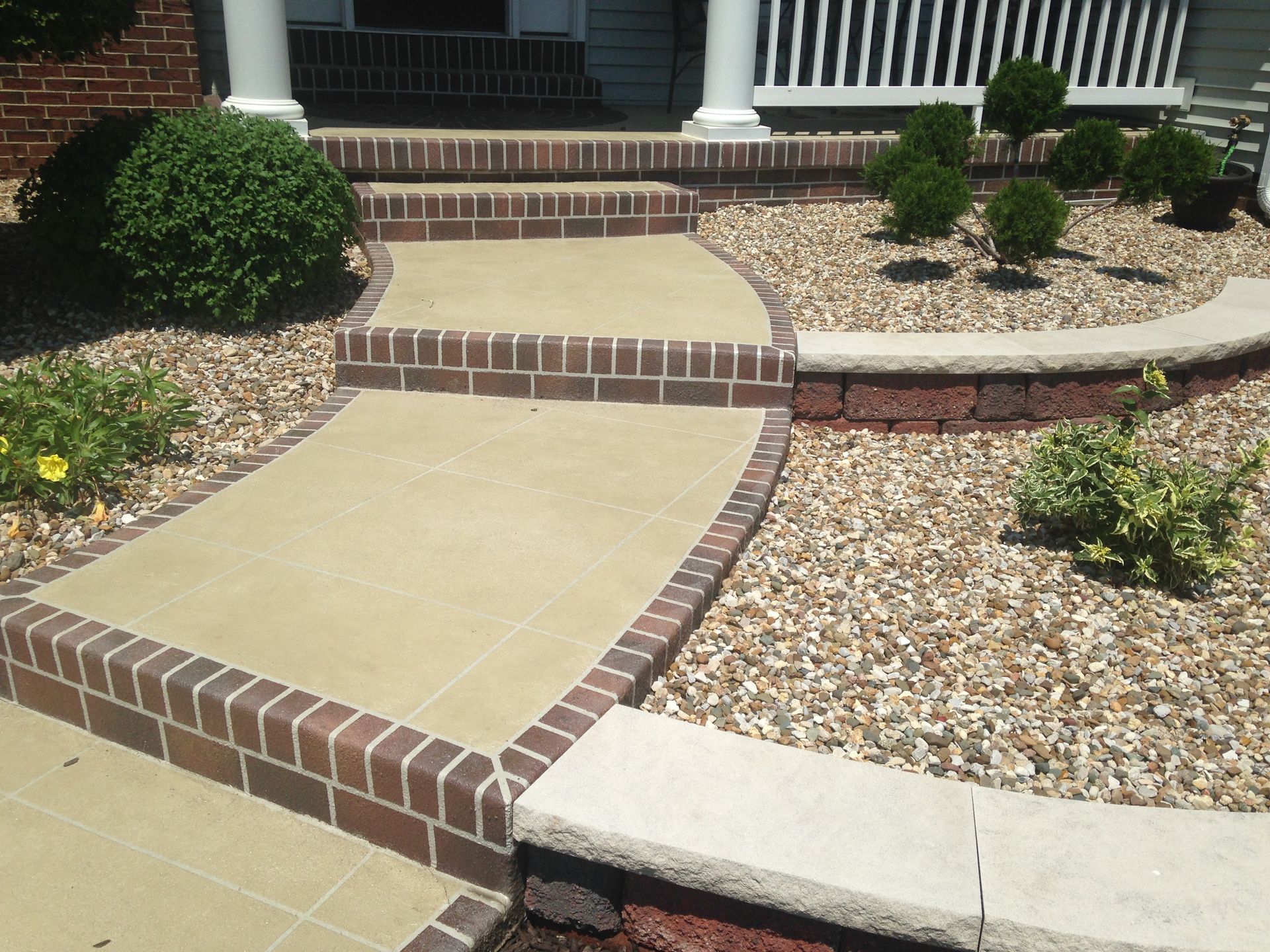 Brick-edged concrete walkway leading to house steps, with flower beds and landscaping.