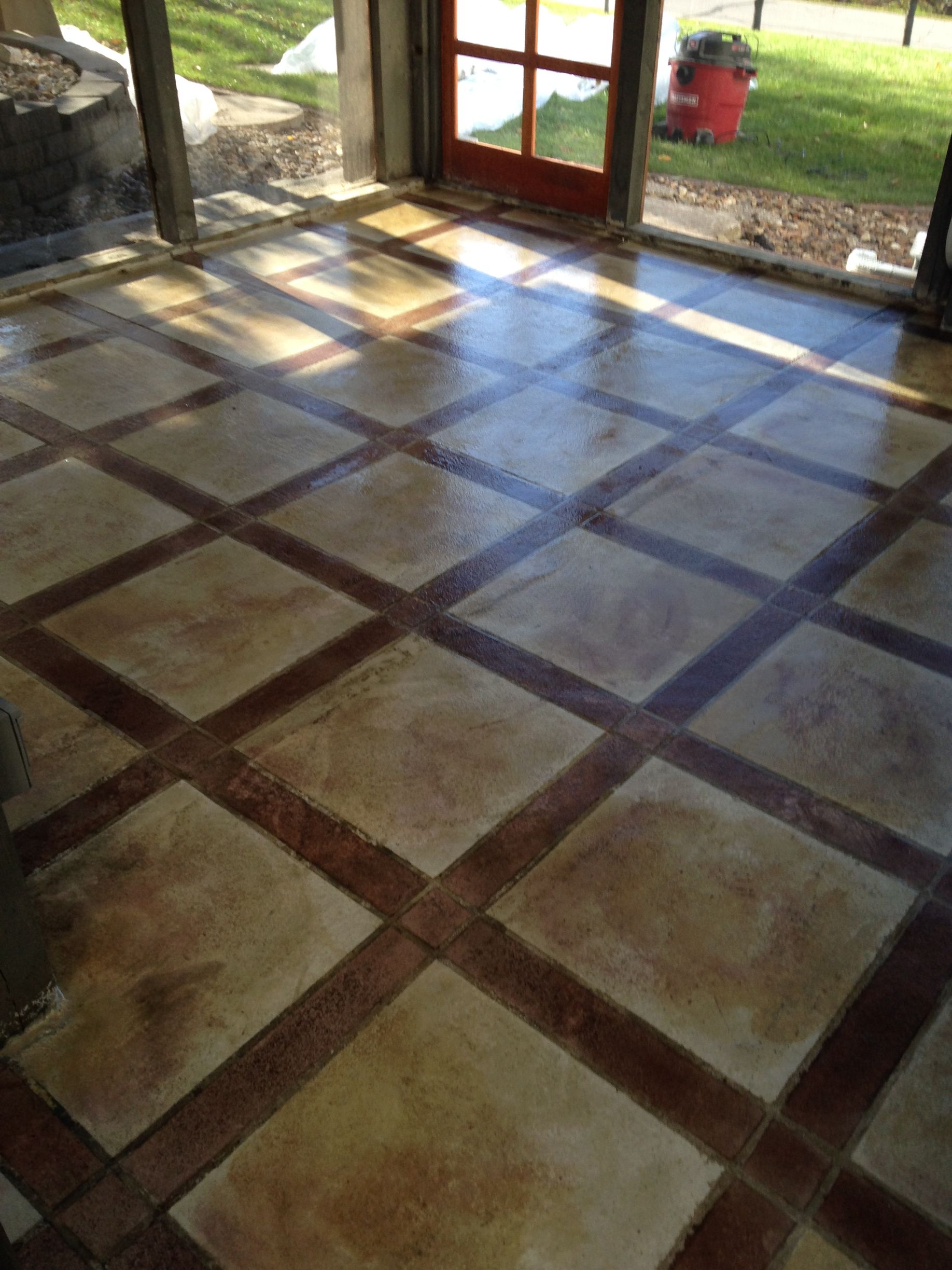 Concrete floor with square tile pattern in brown and tan colors. Light shines through a door.