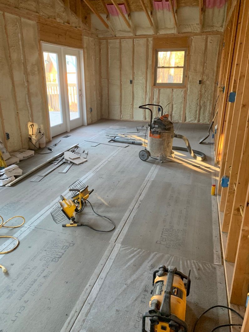 Interior of a room under construction, concrete floor, spray foam insulation, tools scattered.