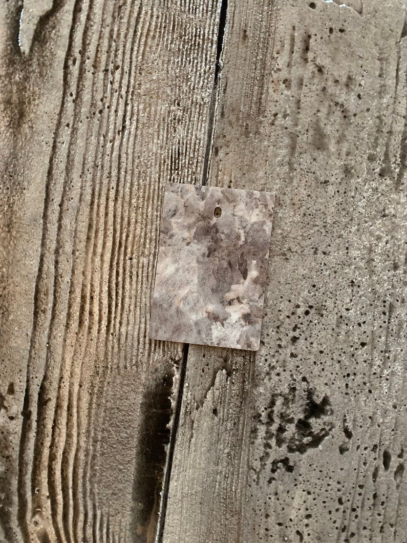 Patchy, gray-toned wood surface with a small, pale square of mottled material adhered to it.