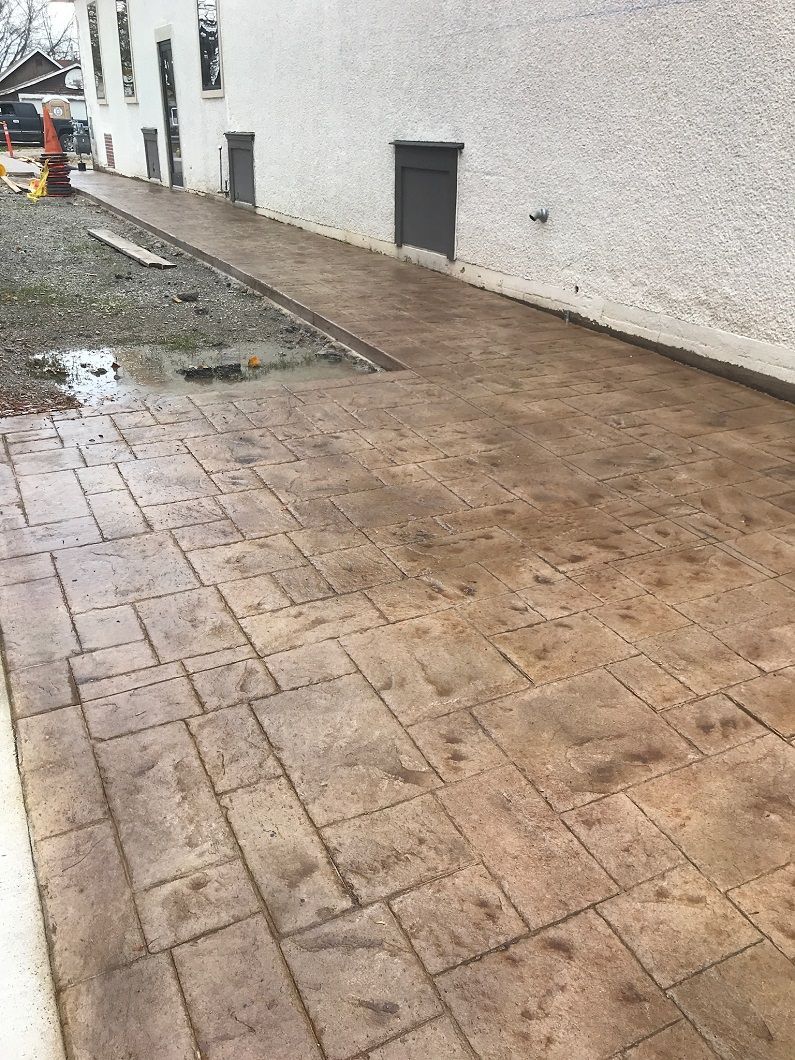Stamped concrete walkway alongside a building with doors. Brown rectangular patterns.