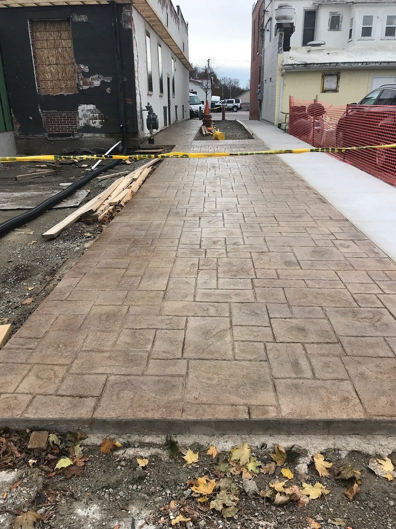 Newly poured concrete sidewalk with a brick pattern in a construction zone.
