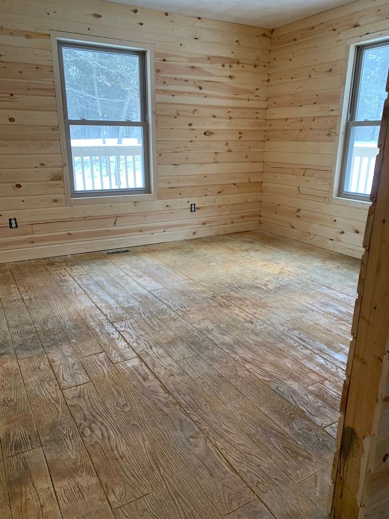 Empty room with wood-paneled walls and floor; two windows.