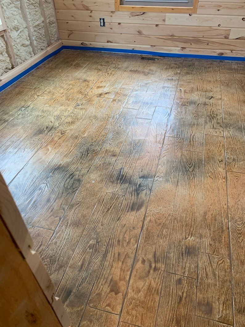 Room with brown and black stained wood floor, blue tape along edges, wooden walls.