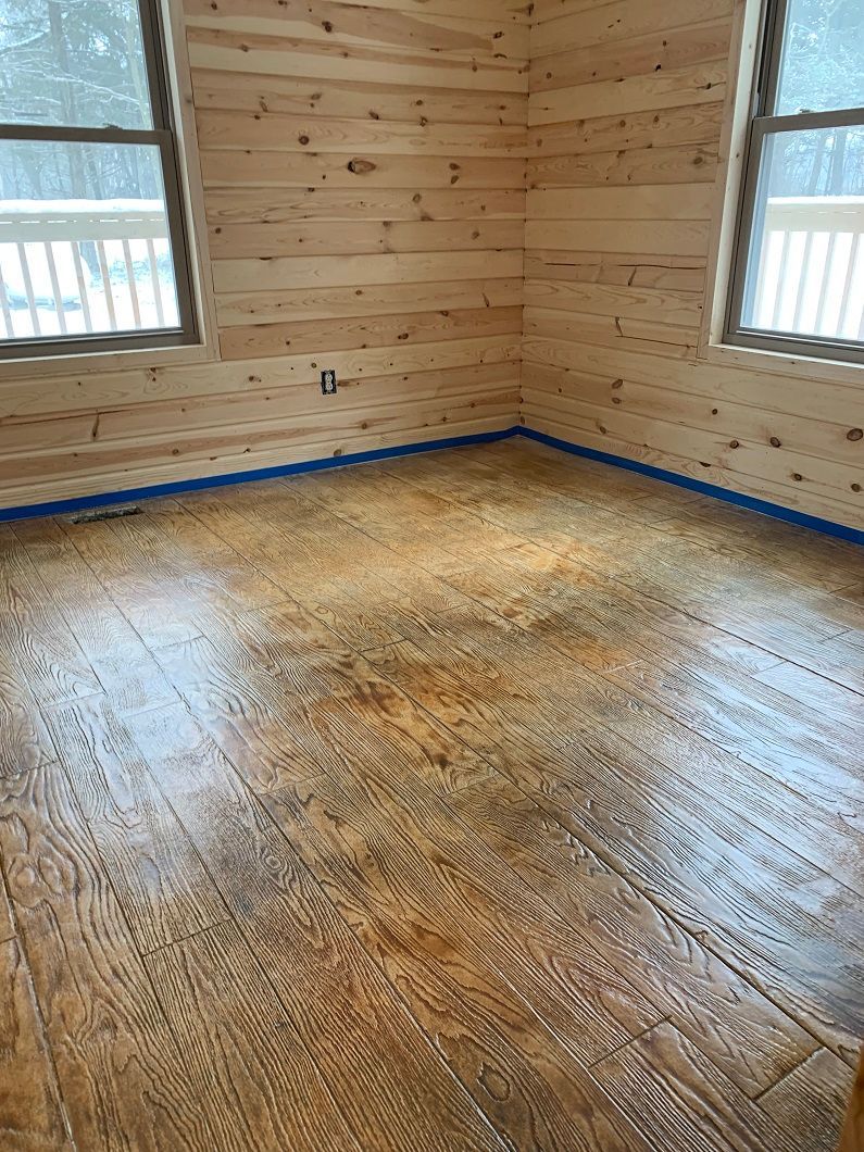 A room with wood-paneled walls and floor, two windows, and blue painter's tape along the floor's perimeter.