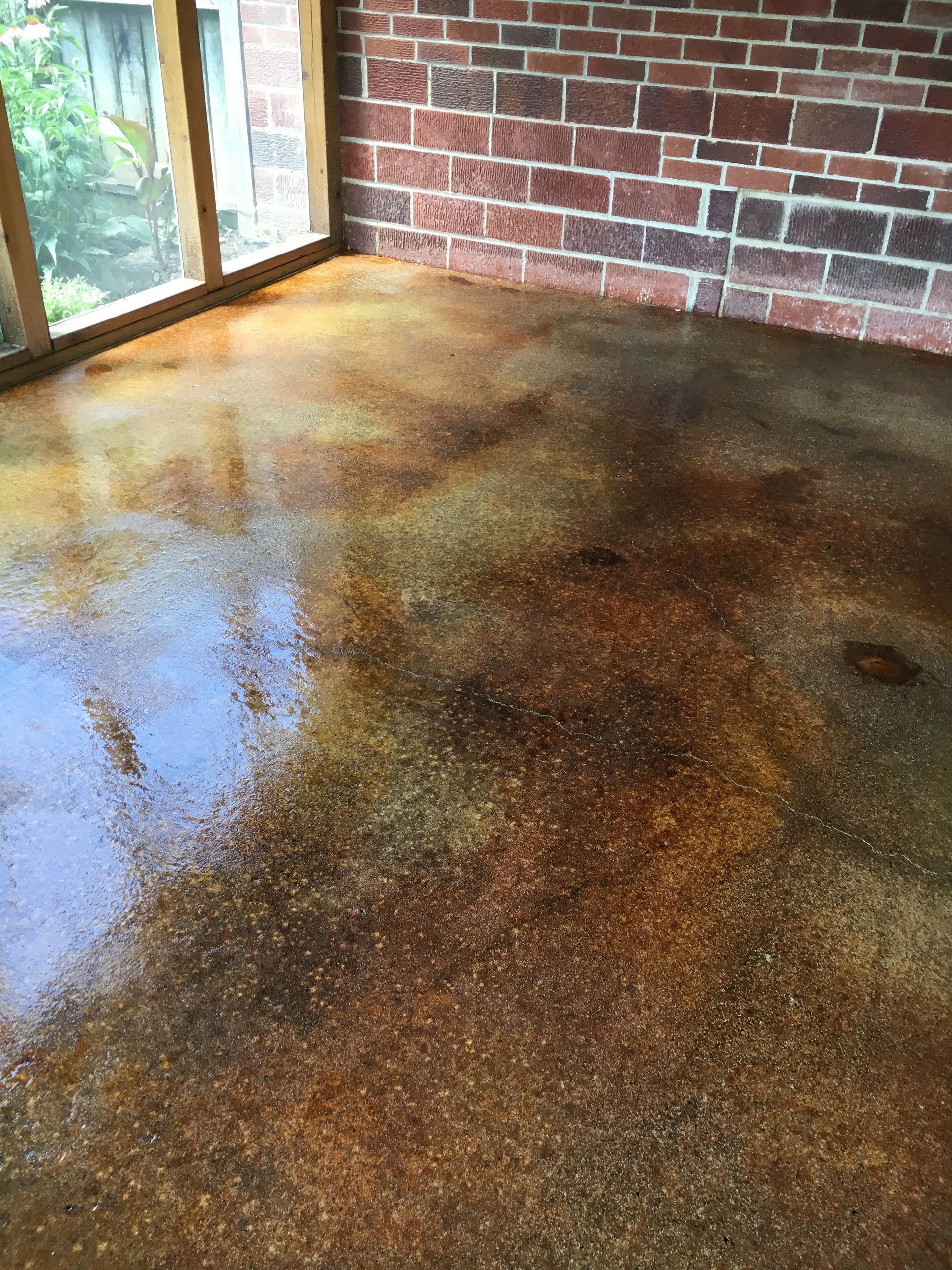 Brown and tan stained concrete floor against a brick wall, lit by window light.