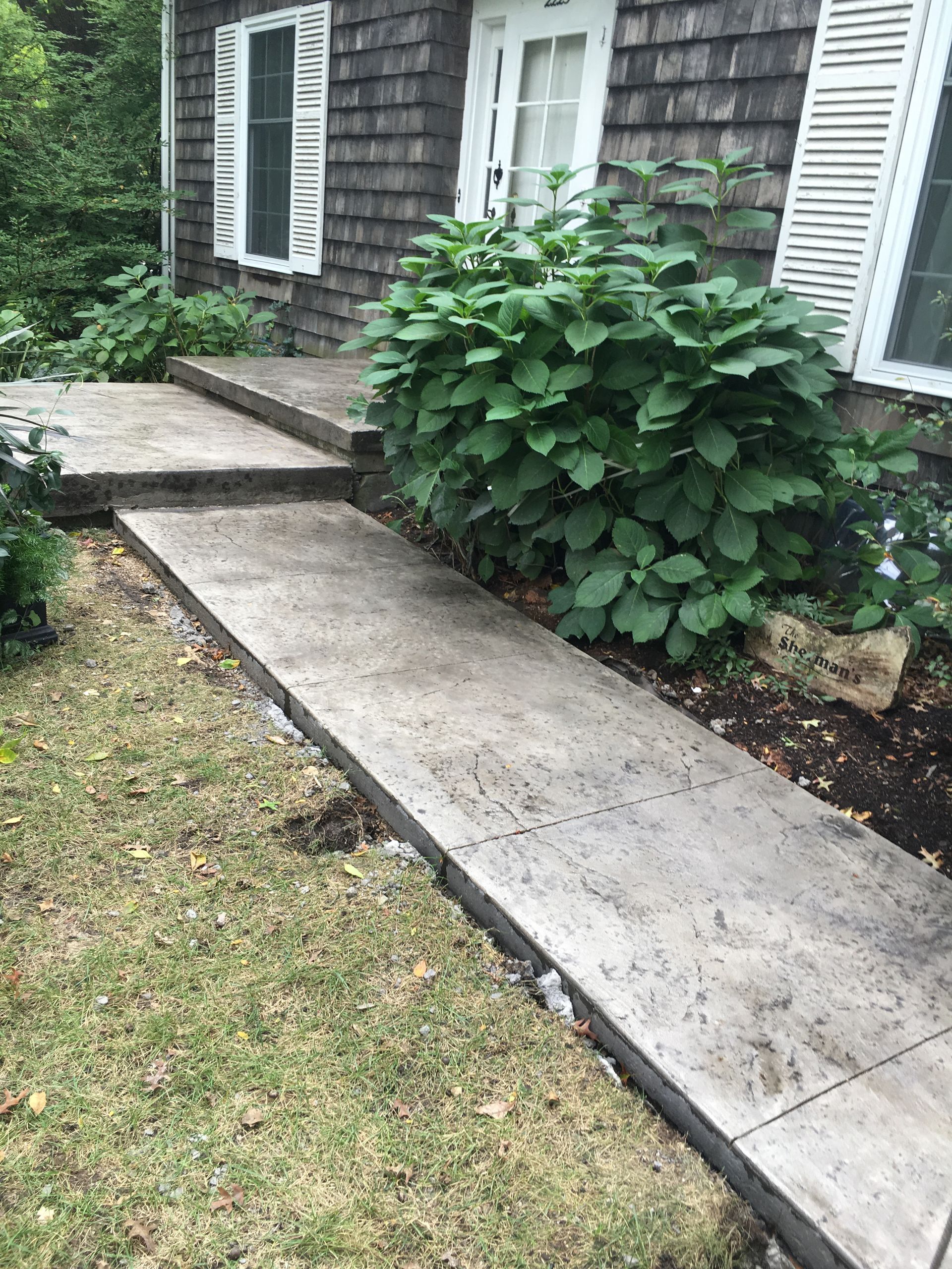 Concrete pathway leading to a house entrance, steps up, green plants.