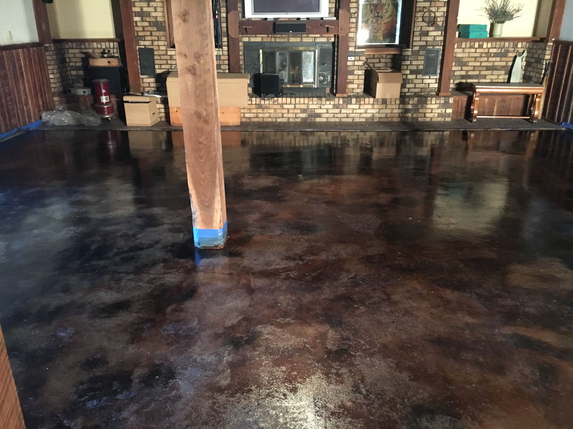 Brown and black stained concrete floor in a room with a fireplace, wood beams, and trim.