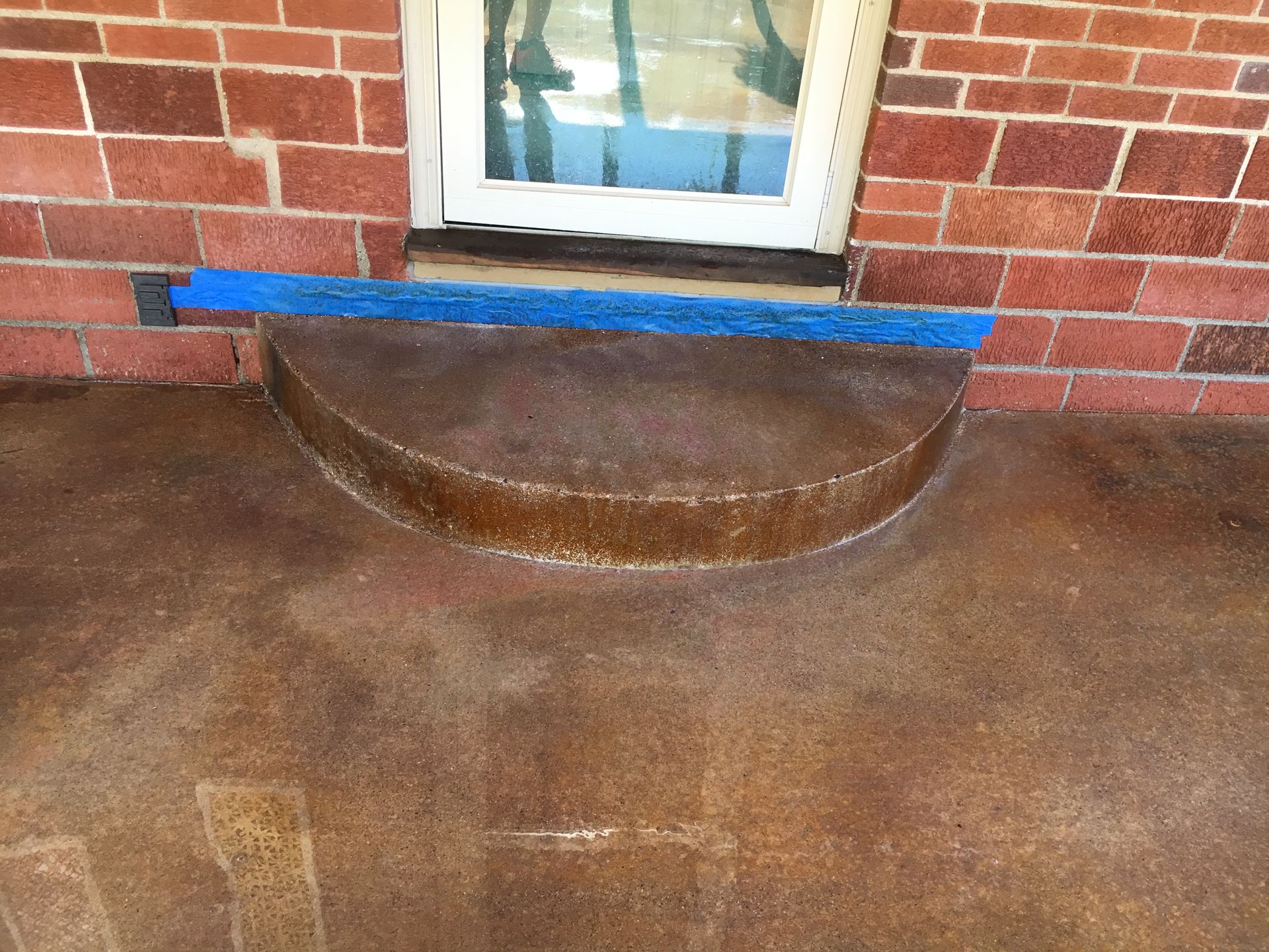 A weathered concrete step in front of a red brick building and a blue mat at the door.