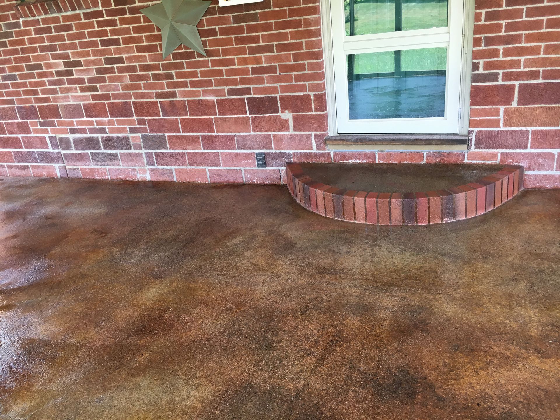 Brick building exterior with stained concrete floor and small brick step leading to a white-framed window.