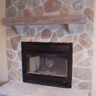 Fireplace with stone facing, dark metal firebox, and wooden mantel.