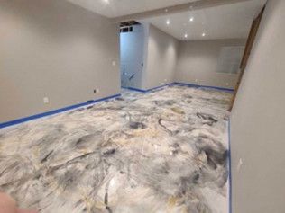 Basement with epoxy floor in silver, black, and gold swirls; blue tape along edges.
