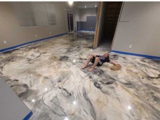 Person on epoxy floor, room with finished marble-like pattern, wearing black, arms outstretched, light reflecting from floor.