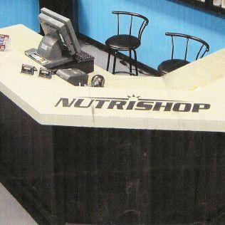 NutriShop store counter with a cash register, two black chairs, and blue wall in the background.