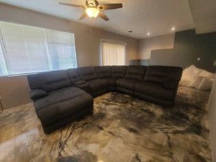 A dark grey sectional sofa in a room with a patterned, reflective floor and a ceiling fan.