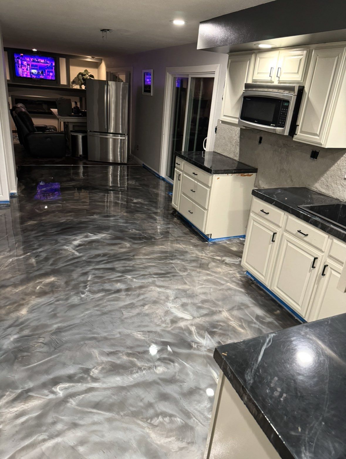 Kitchen with glossy, marbled-looking floor, white cabinets, black countertops, and a stainless steel refrigerator.