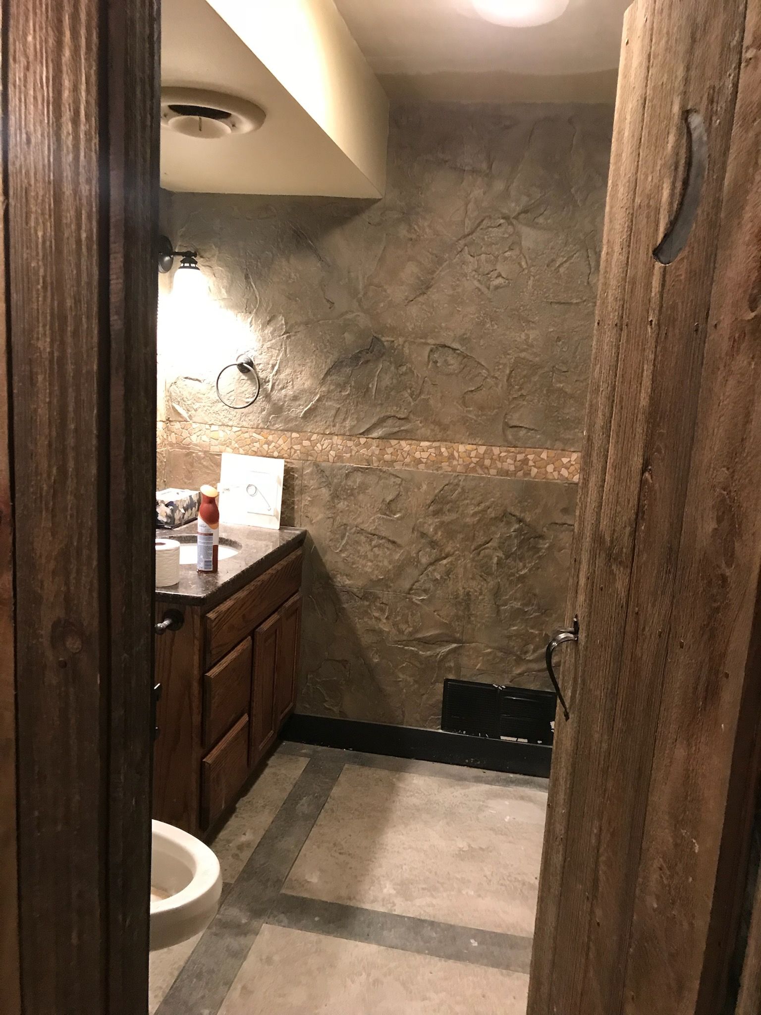 Bathroom with rustic wooden door, stone walls, wood vanity, and toilet.