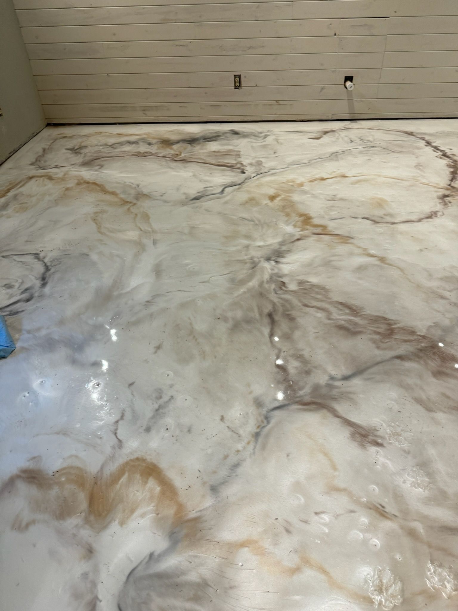 Marble-effect epoxy floor in white and beige with brown veining. Located in a room with wood-paneled ceiling.