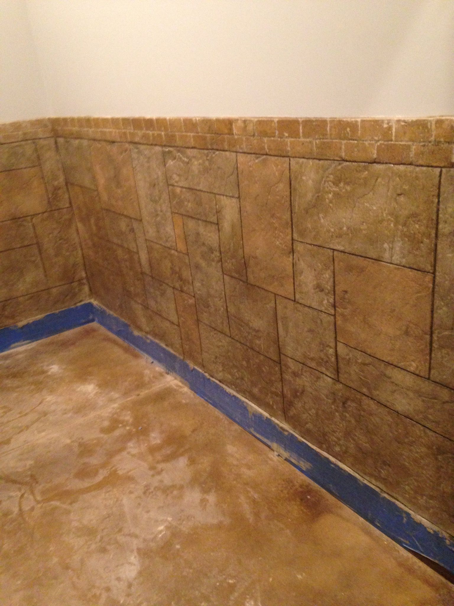 Stone-textured wall with blue trim along the bottom. Brown concrete floor with white wall above.