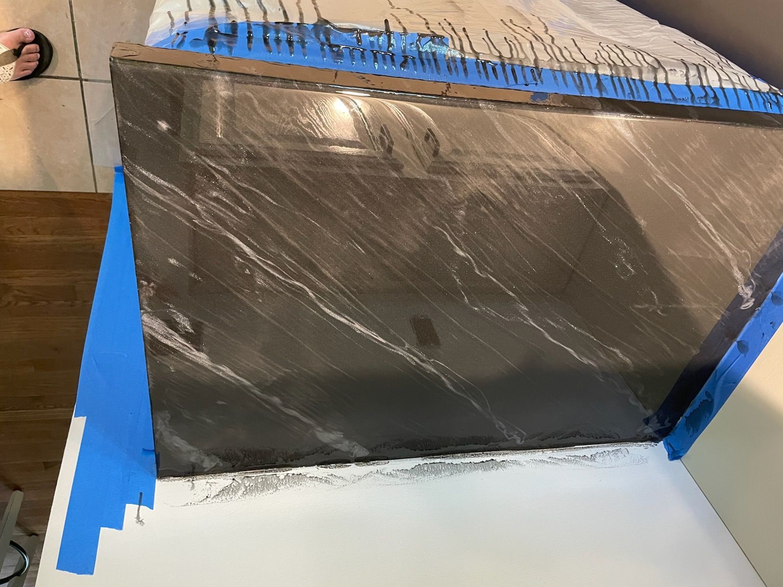 Dark countertop with white veining, taped, being installed over white cabinets.