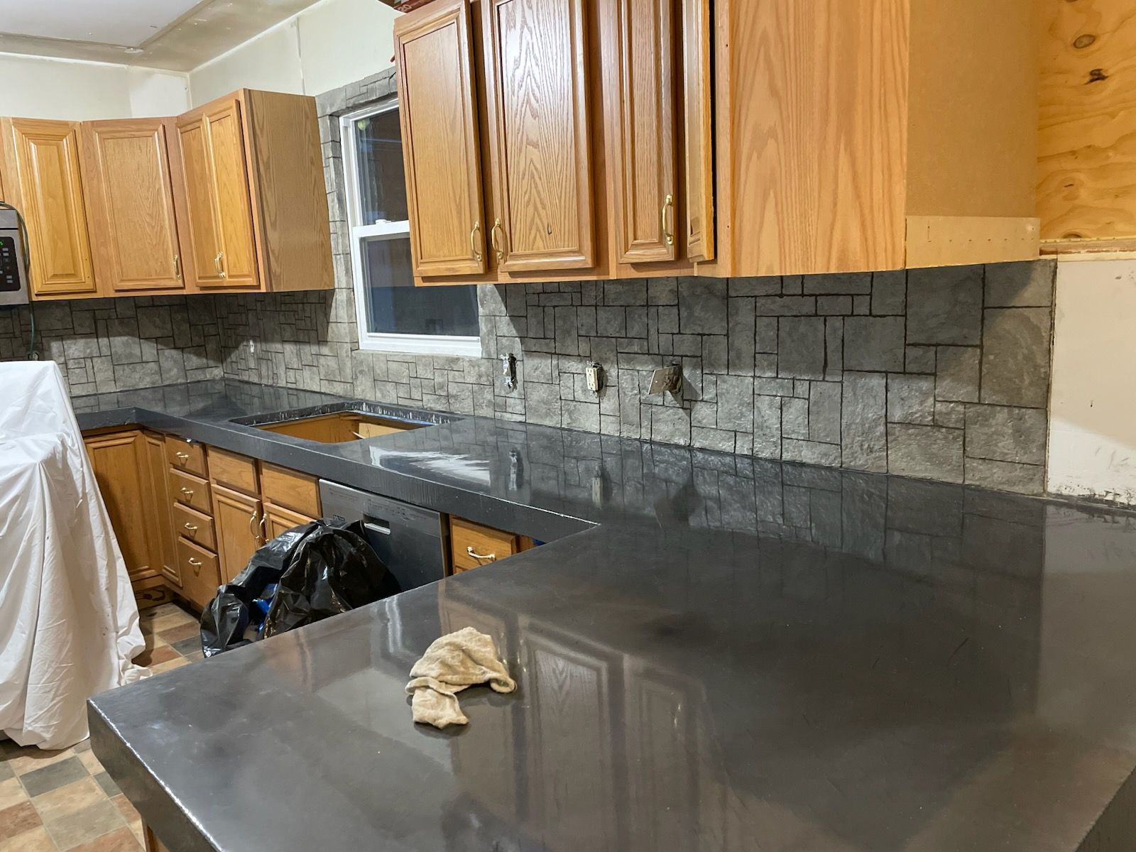Kitchen renovation in progress with gray countertops, stone backsplash, and wooden cabinets.