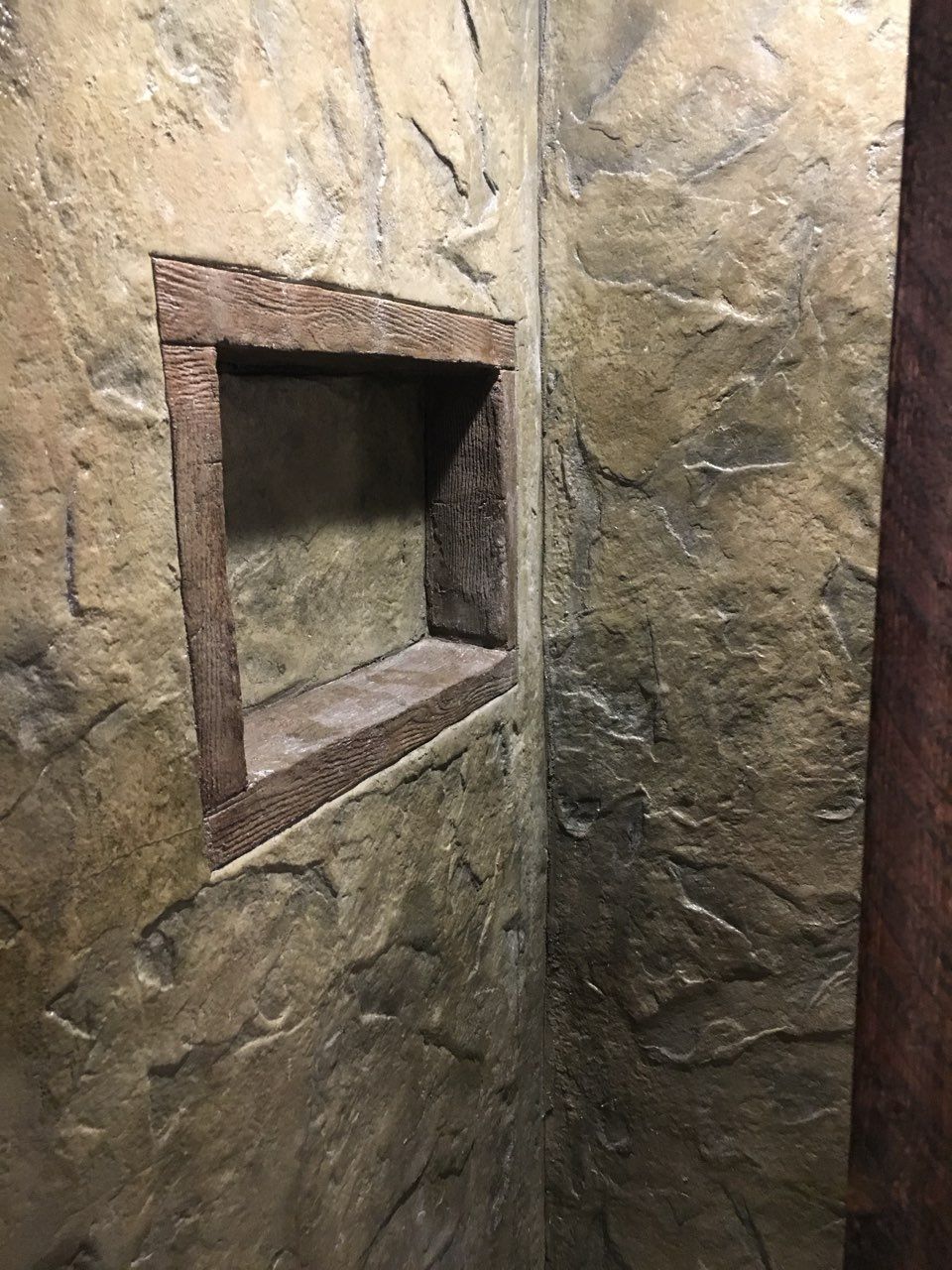 Stone-textured shower wall with a recessed shelf, featuring varying shades of brown and gray.