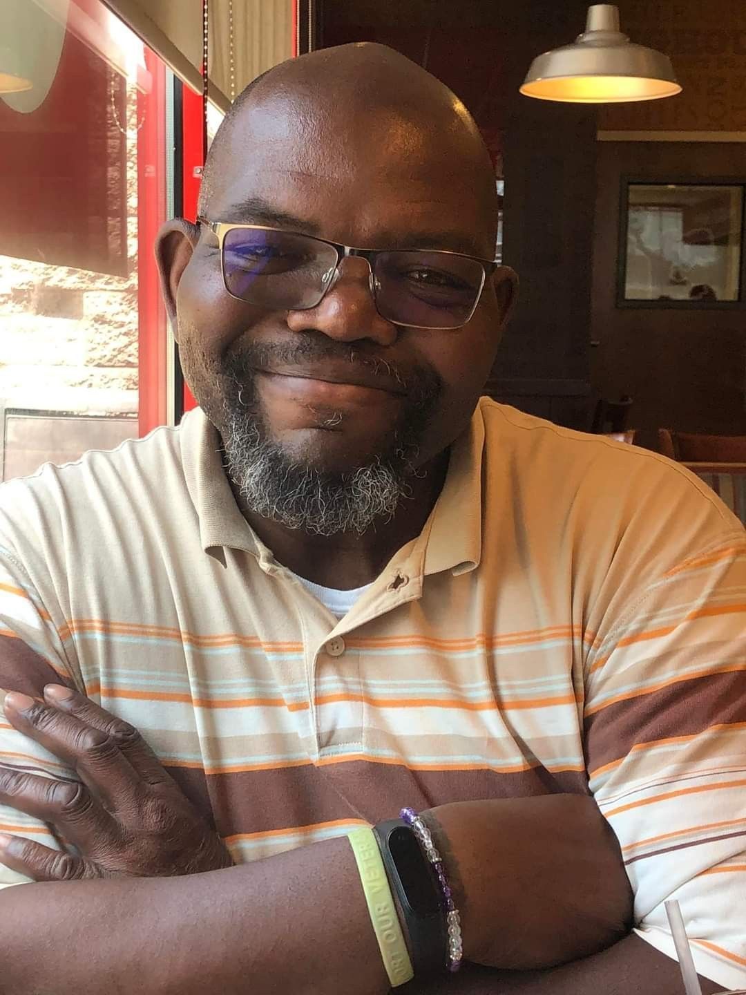 A man with glasses and a beard is sitting at a table with his arms crossed.