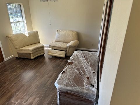 A living room with two chairs and a couch wrapped in plastic.