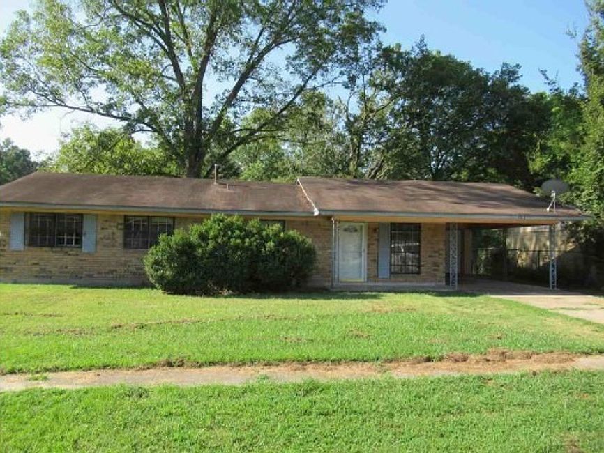 A brick house with a brown roof and a large lawn in front of it