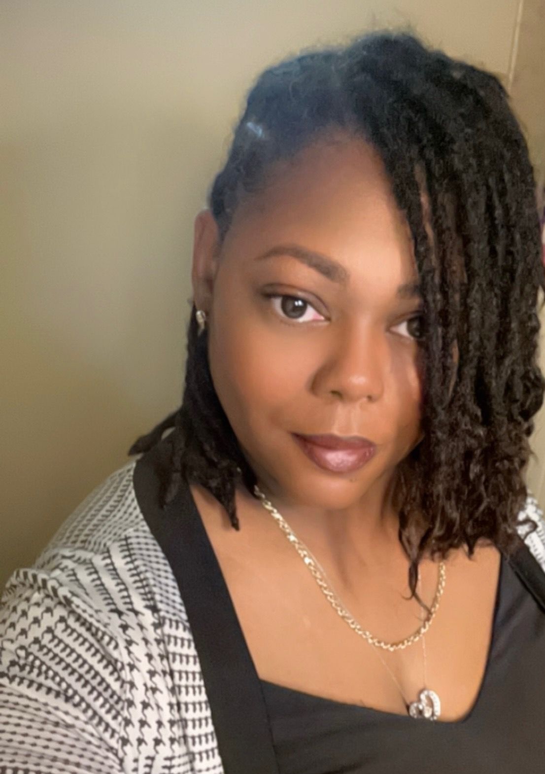 A woman with dreadlocks and a necklace is taking a selfie.