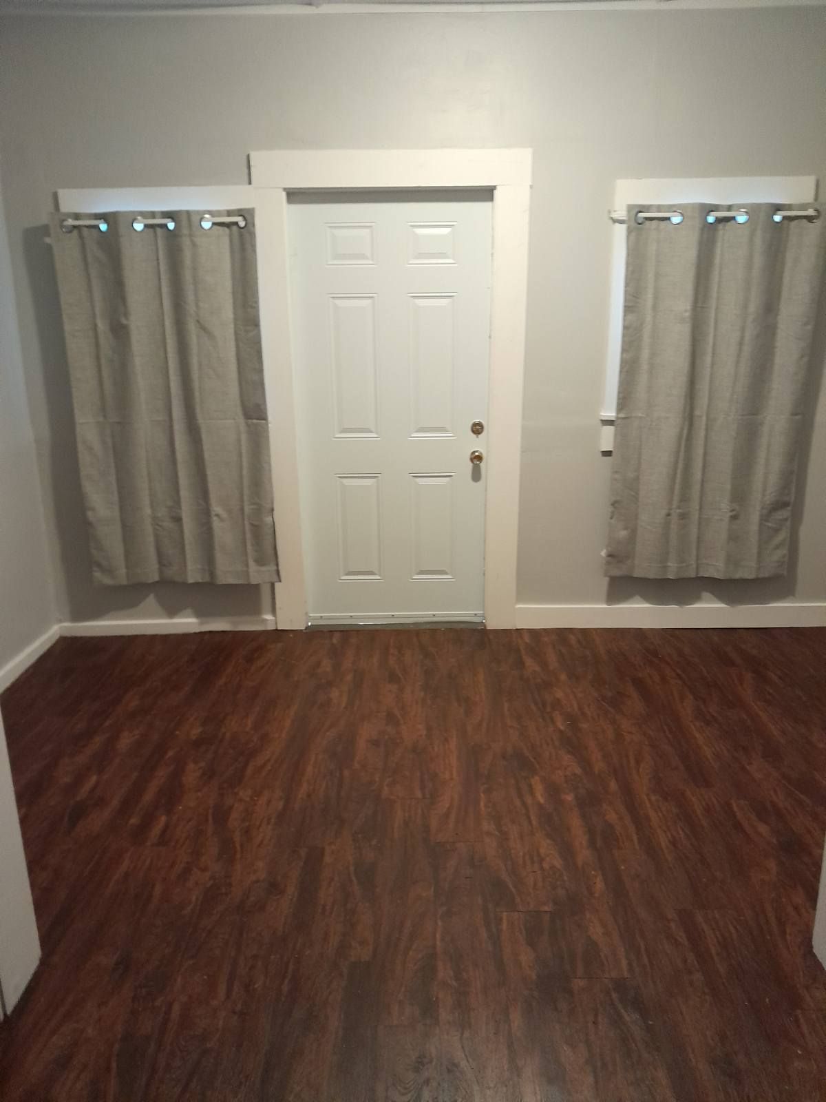A room with hardwood floors , a door and two windows.