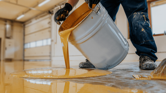 Worker tilting a bucket to spread thick epoxy coating across a floor, forming a durable finish during an epoxy flooring service in Scottsdale, AZ
