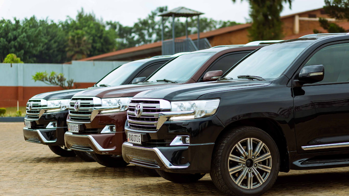 Four luxury SUVs parked side-by-side, in shades of silver, burgundy, and black. Outdoors, near a low wall.