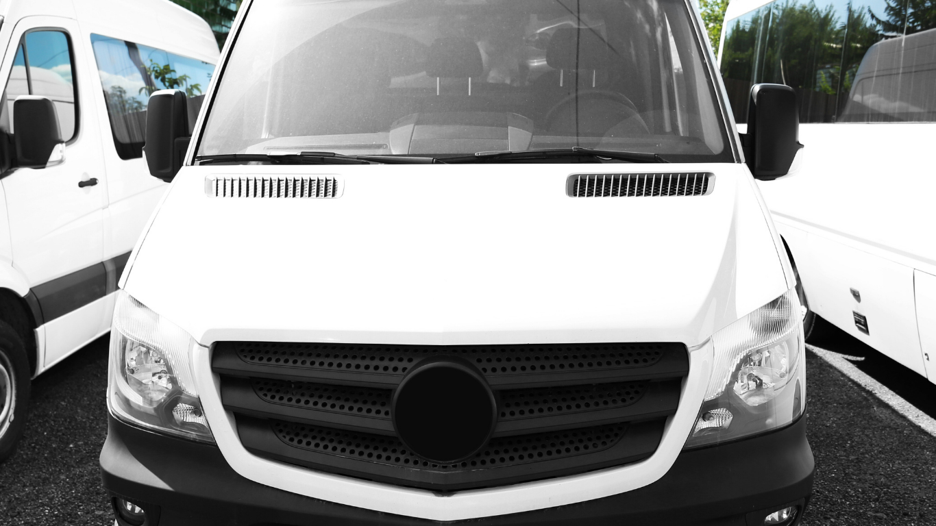 White van parked in a lot, viewed from the front. Other vans visible in the background.