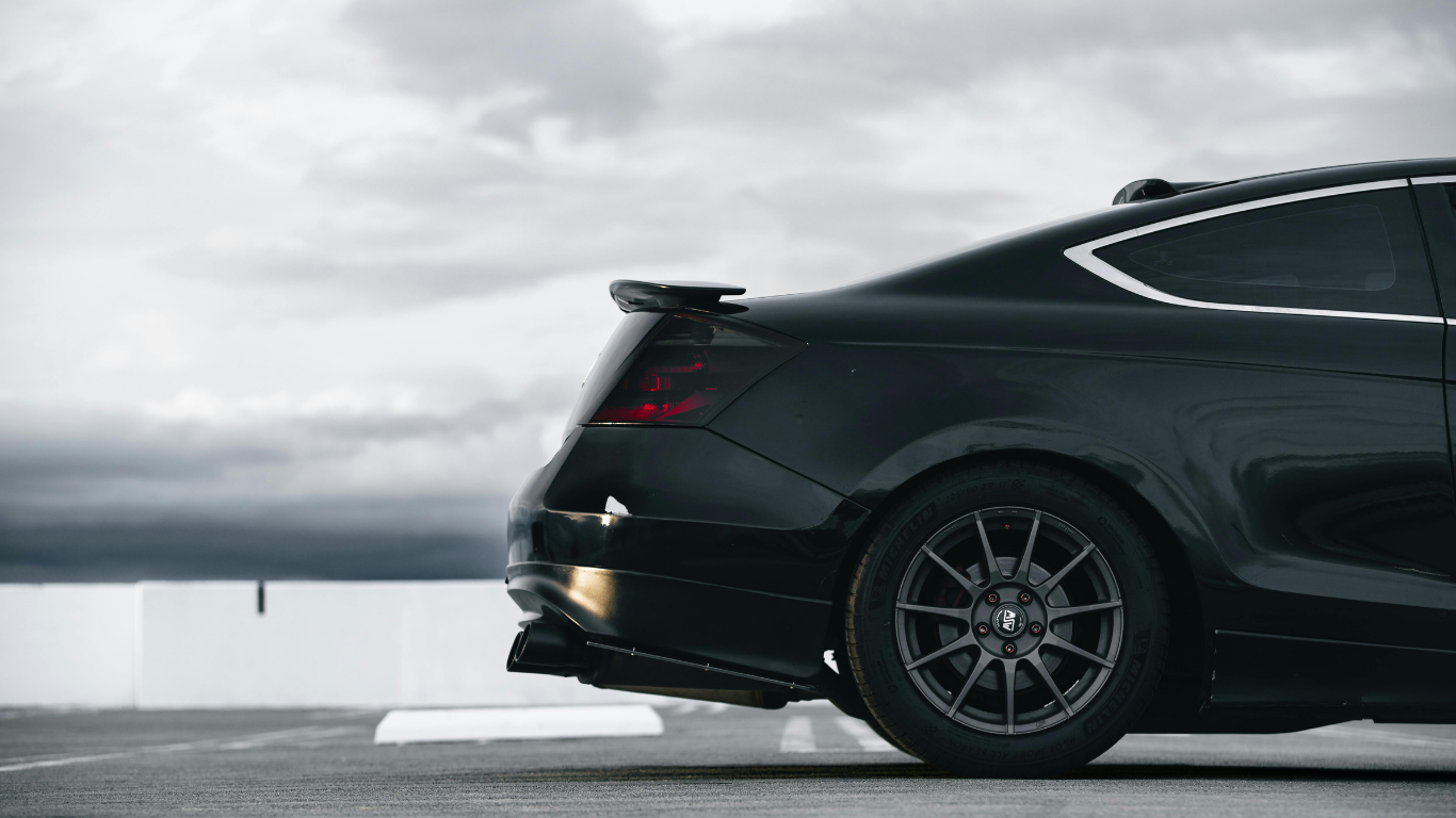 Black coupe car, rear view, parked on a rooftop against a cloudy sky.