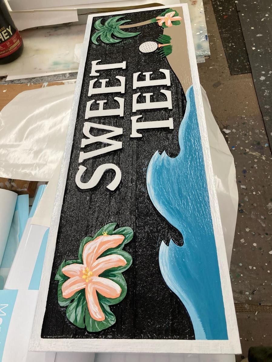 Sweet Tee sign on a black tabletop with blue wave design and palm tree decorations