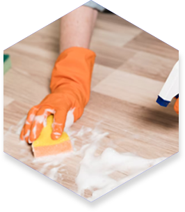 Person wearing orange gloves cleans a wooden floor with a sponge and cleaning solution.