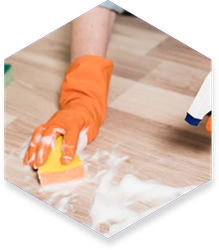 Person wearing orange gloves cleans a wooden floor with a sponge and cleaning solution.