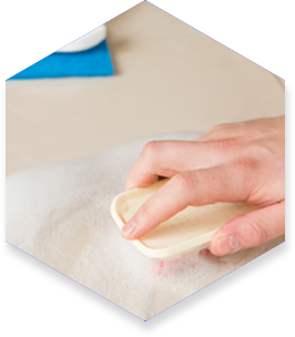 A person's hand gently brushes a white, fluffy surface with a light-colored tool.