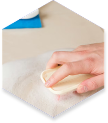 A person's hand gently brushes a white, fluffy surface with a light-colored tool.