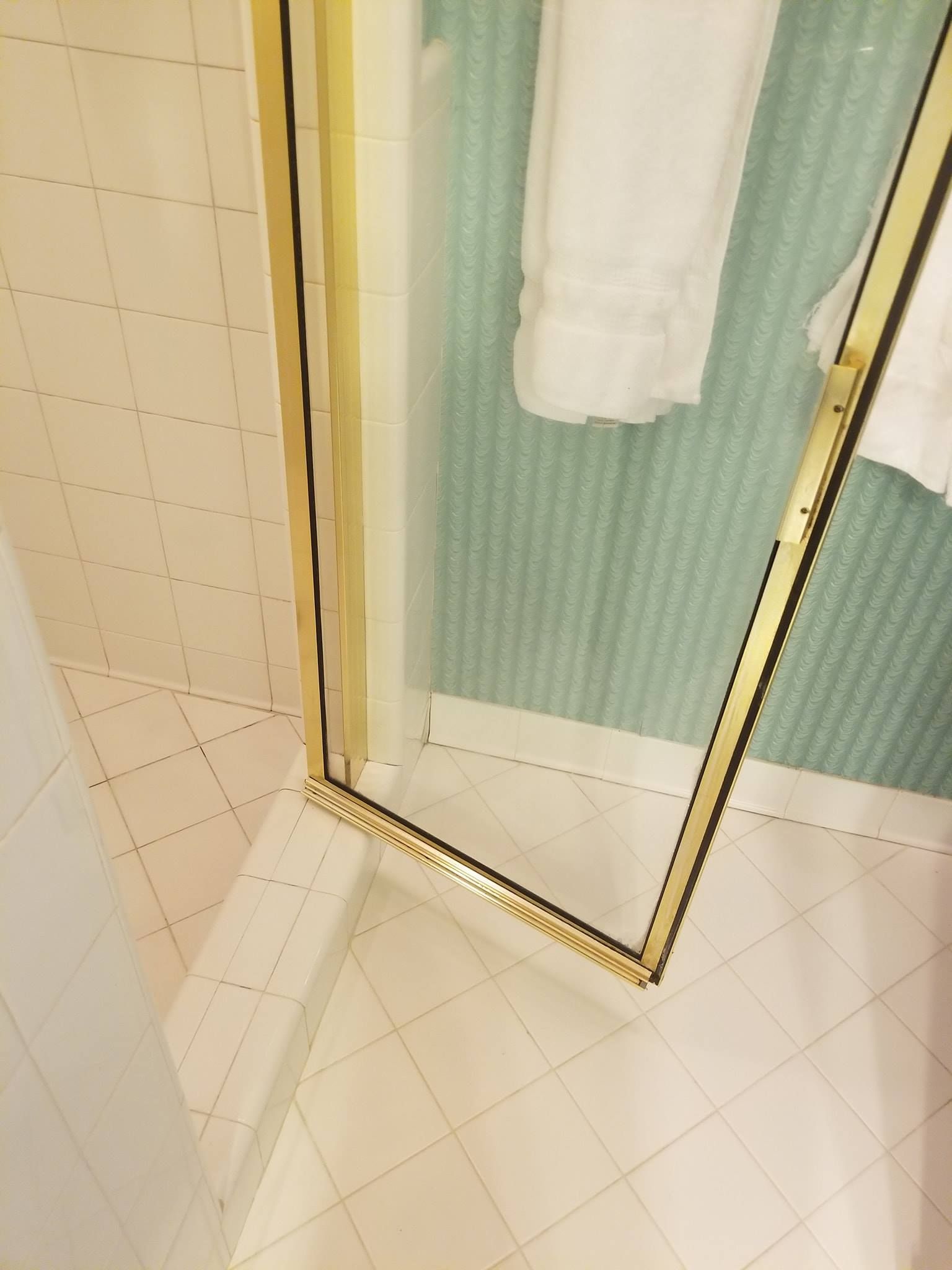 Gold-framed shower door in a corner, with white tiled floor. White towels hang on a blue-green textured wall.