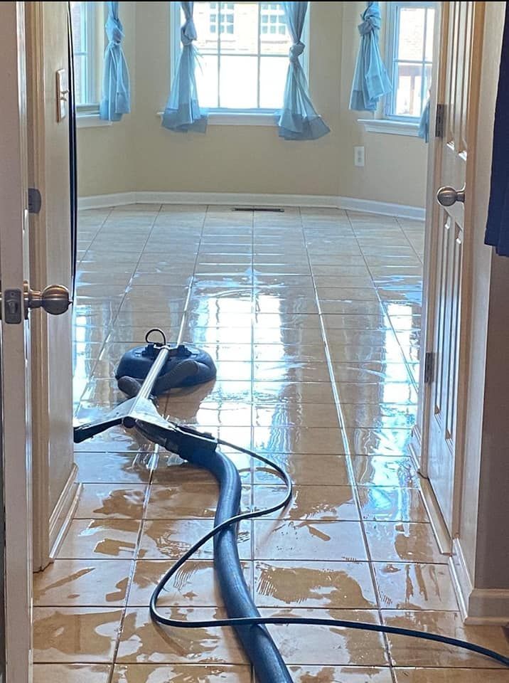 A wet tile floor being cleaned with a machine, doorway view, blue curtains in the background.