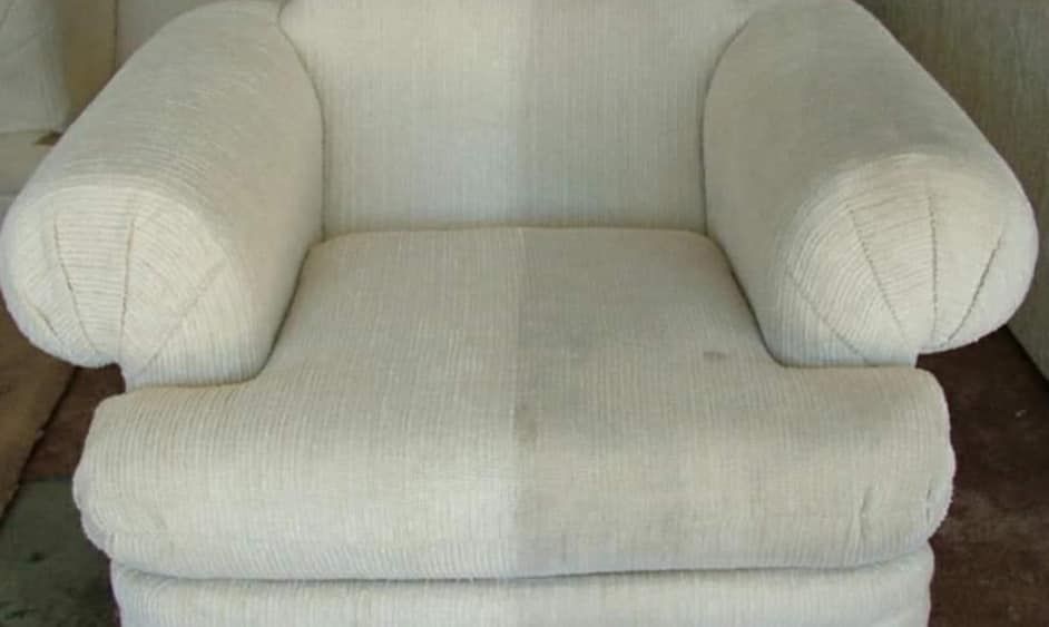A cream-colored armchair, half-cleaned, showing contrast between dirty and clean sides.